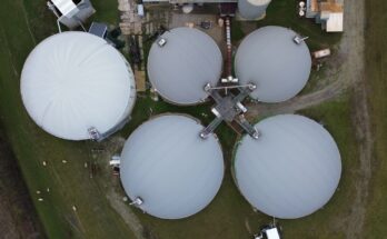 a group of large white tanks sitting on top of a lush green field. Biogas